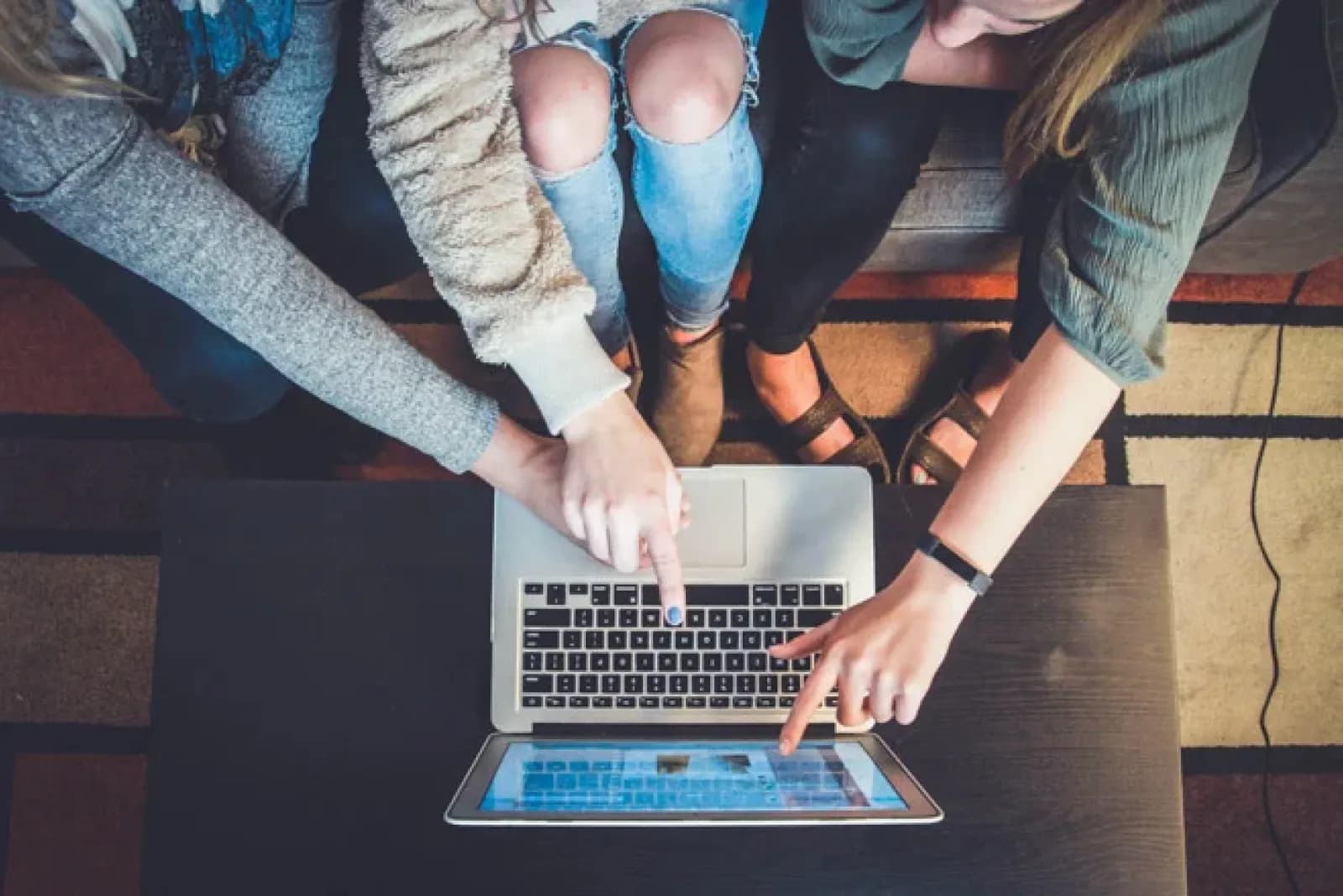 3 friends sitting by a laptop and pointing to a screen