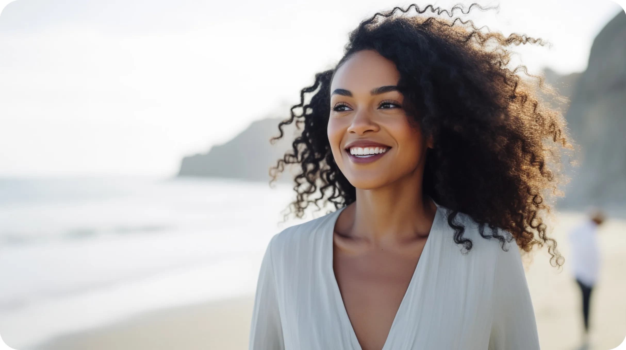A happy woman walking on a beach by a ocean shore with mountains in a background