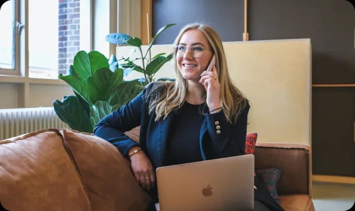 A woman using a laptop and phone while sitting on a couch.