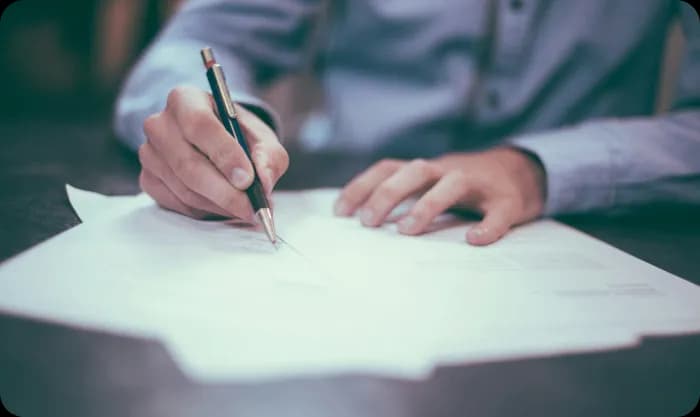Man holding a pen and signing documents on table