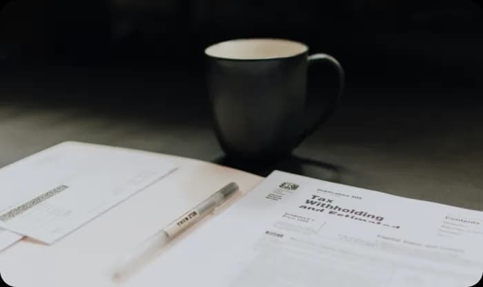 A desk with a coffee mug and for state forms on it.