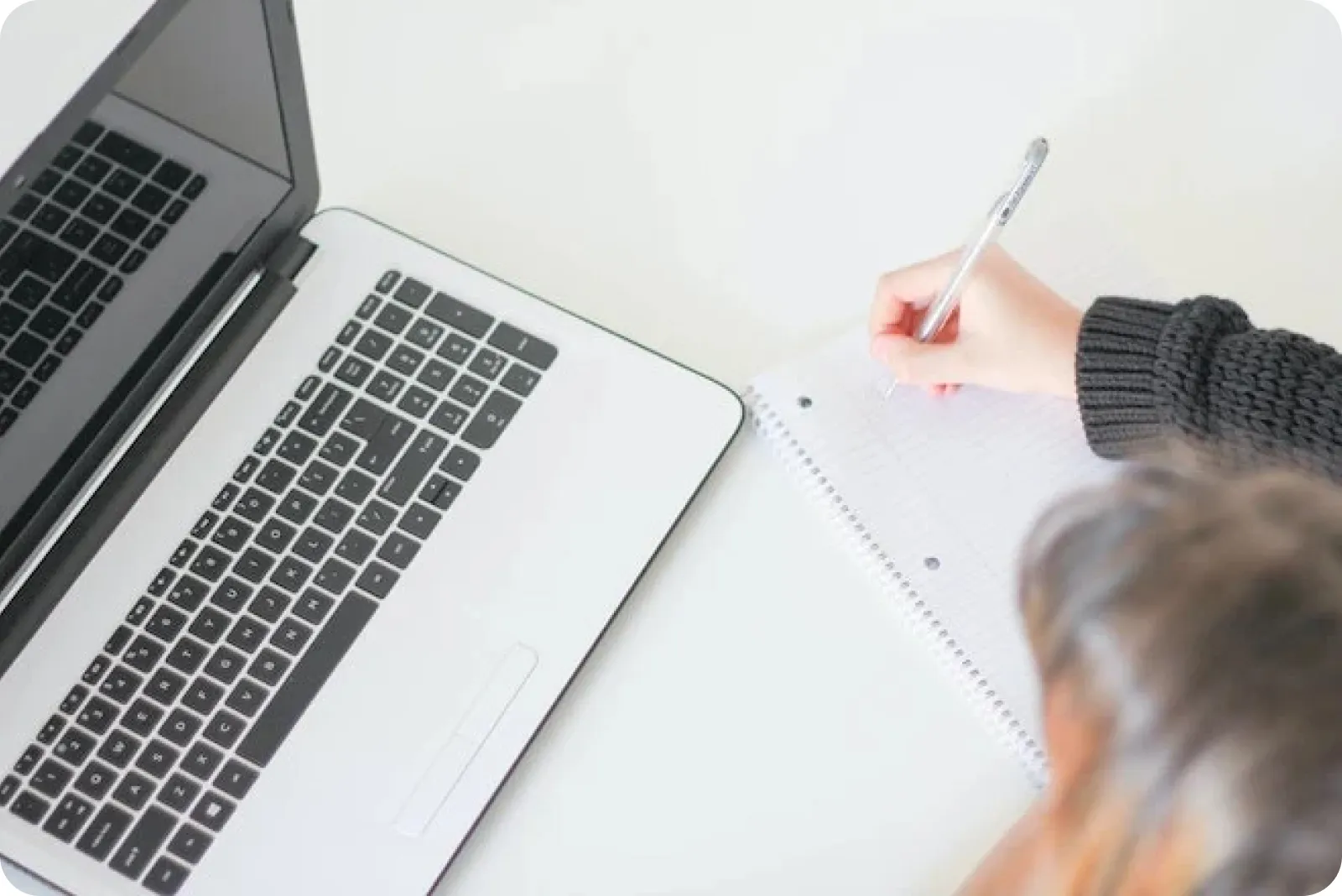 Woman writing on a paper while working on a Laptop