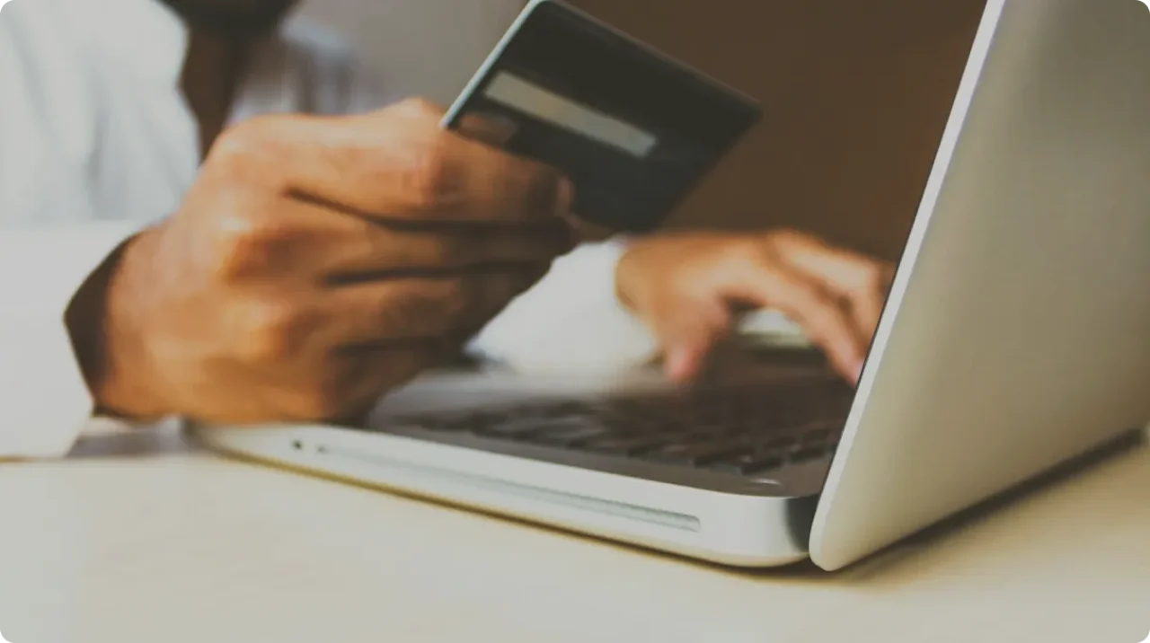 A person wearing a white shirt is using a laptop while holding a credit card in their hand