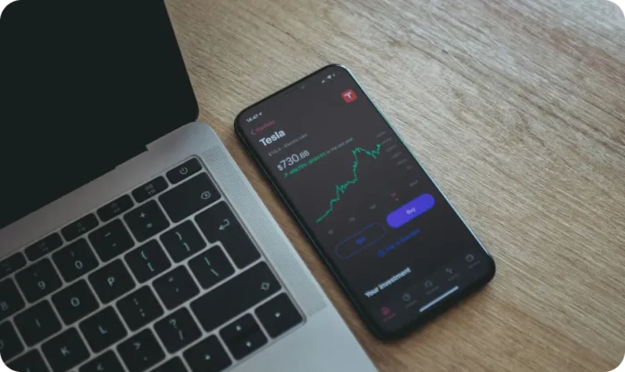 Smartphone displaying Tesla stock chart next to a laptop.